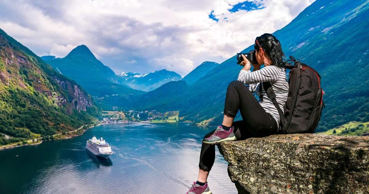 female traveler taking photos of mountains on cliff edge 